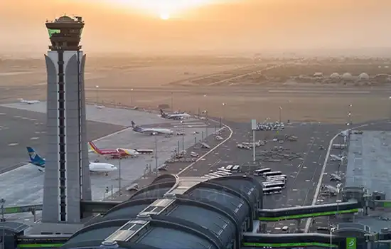 An image of Muscat International Airport's control tower and runway at sunset, with several parked aircraft.