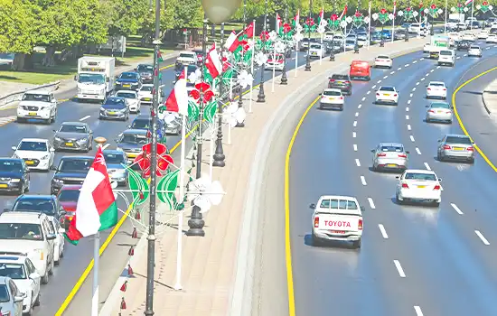Oman Gears Up for 54th National Day 4 An image of a street in Oman adorned with LED lights in the colors of the Omani flag (green, red, white), with vehicles decorated with Omani flags driving along the road.