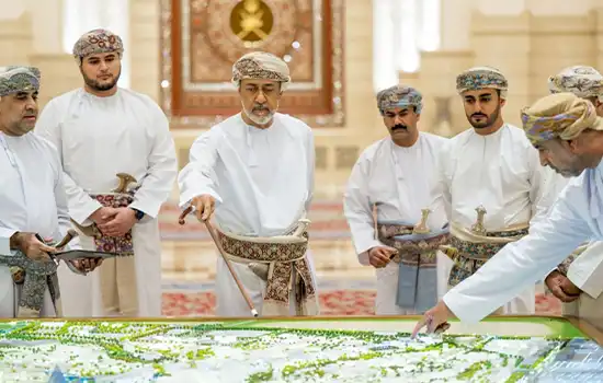 An image of the Sultan of Oman reviewing a map with a group of officials beside him.