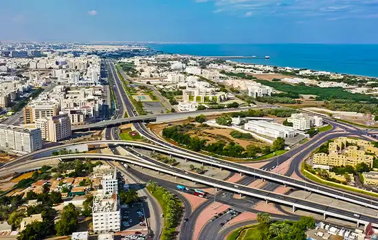 An aerial view of a complex highway in Oman with buildings and the ocean in the background