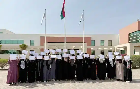A group of Afghan female students standing in the courtyard of the Middle East College in Oman, holding placards in protest to protect their right to education.