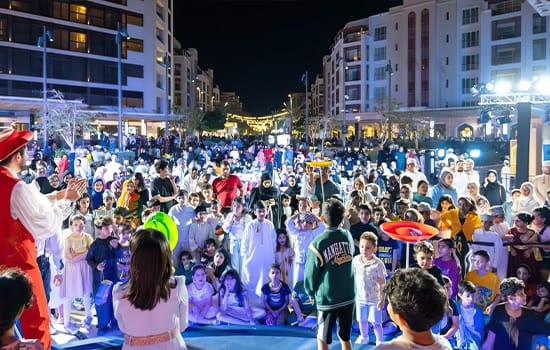A large crowd enjoying a vibrant street performance at Al Mouj Walk in Muscat at night