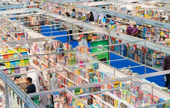 Overhead view of publisher booths filled with colorful books and visitors at the Muscat International Book Fair 2025