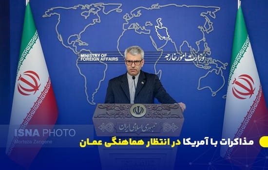 سخنگوی وزارت خارجه ایران در نشست خبری درباره مذاکرات ایران و آمریکا، با اشاره به نقش عمان در هماهنگی‌ها. پشت تریبون وزارت خارجه با نقشه جهان در پس‌زمینه و پرچم‌های ایران.