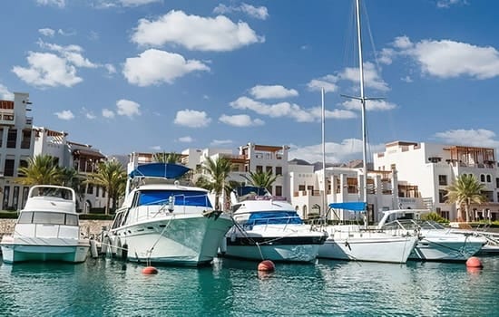 يخوت فاخرة راسية أمام مجمعات سكنية عصرية على الواجهة البحرية في عمان